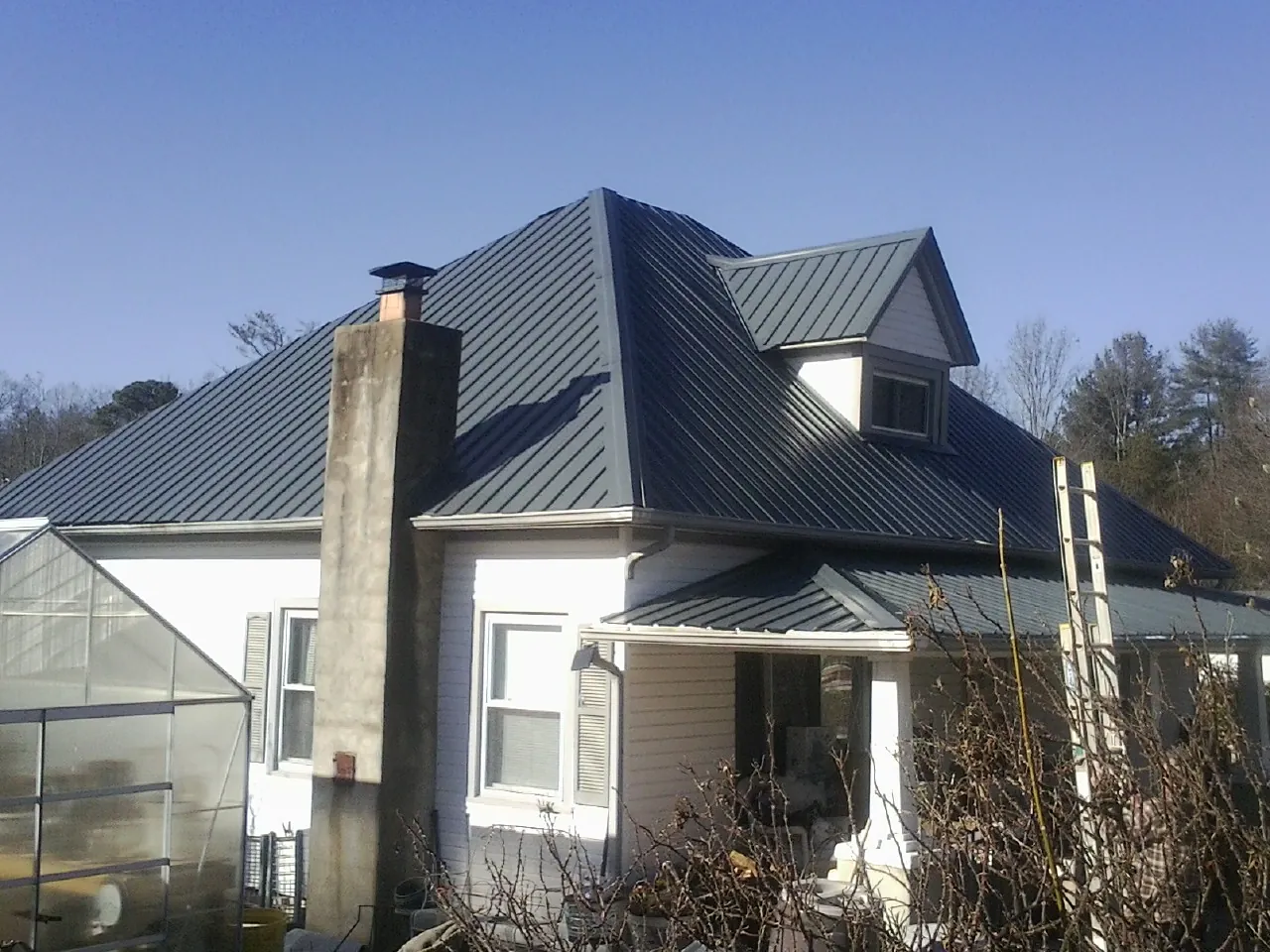 Dark blue standing seam metal roof on a white farmhouse with dormer — Slate & Tile Roof Repair by Roofing Brothers in Bunch
