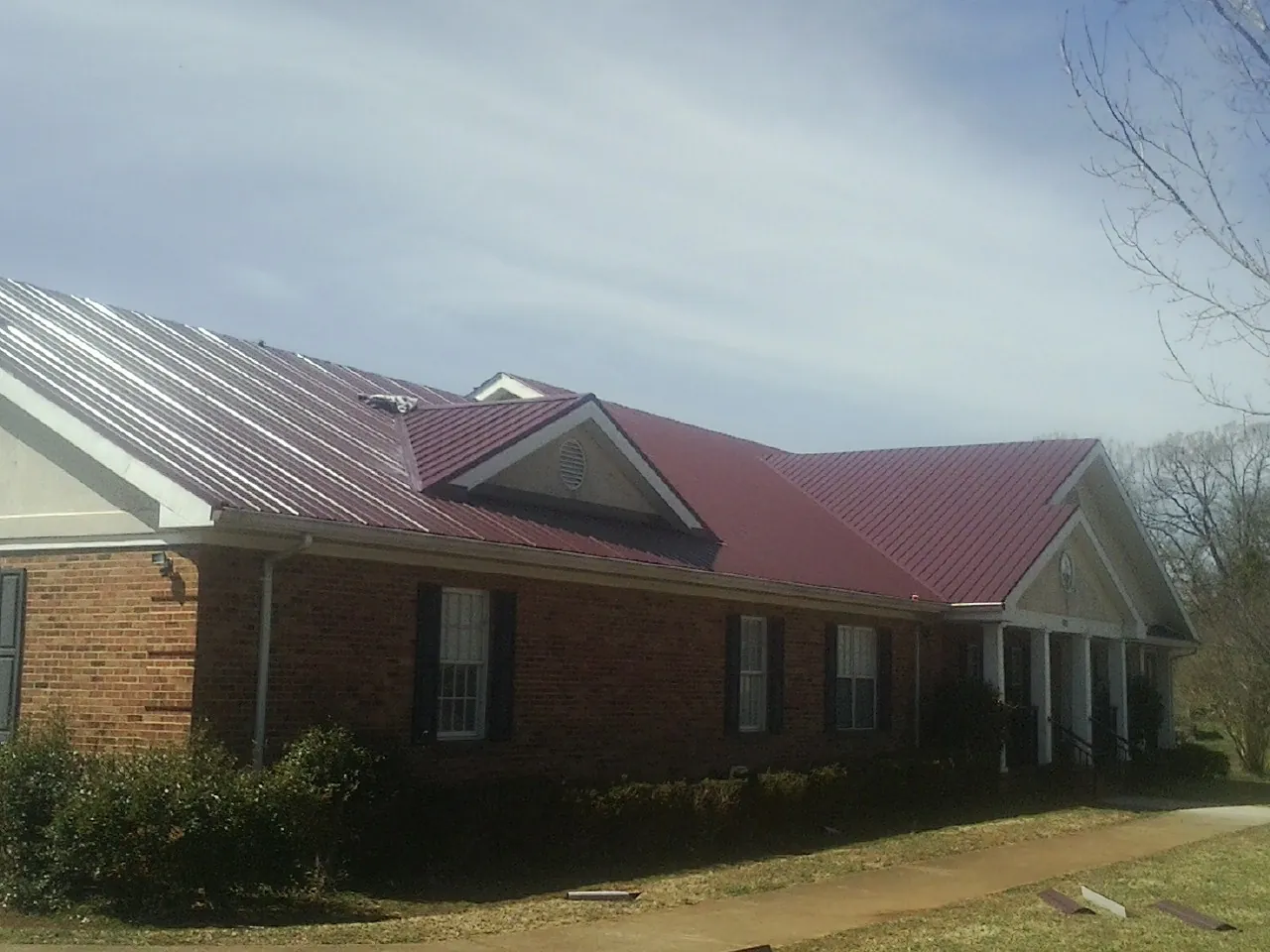 Red metal roof with gabled entries on a long brick building, from a Hail Damage Roof Repair job in Bunch
