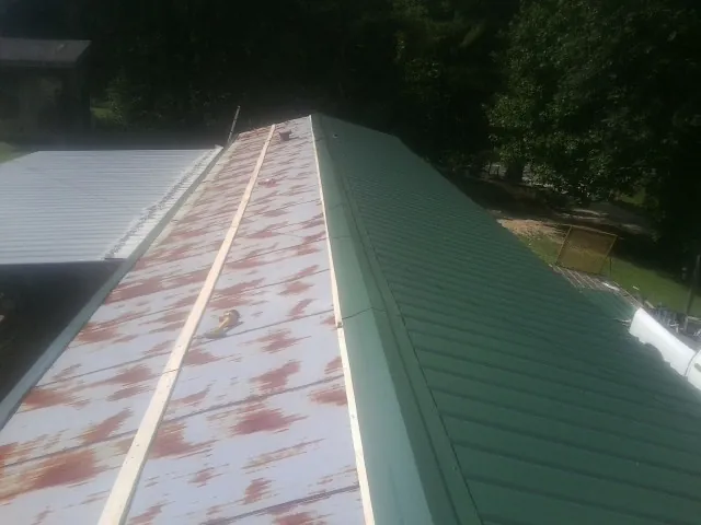 Old rusted panels beside newly installed green metal roofing — Wind Damage Roof Repair by Roofing Brothers in Bunch
