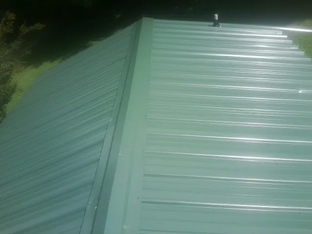 New green metal panels meeting at the ridge of a roof — Flat Roof Repair work by our crew in Bunch