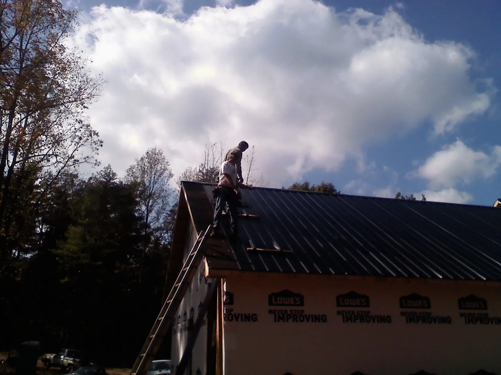 Roofer fastening dark metal panels high against a cloudy sky, from a Roof Inspection job in Bunch