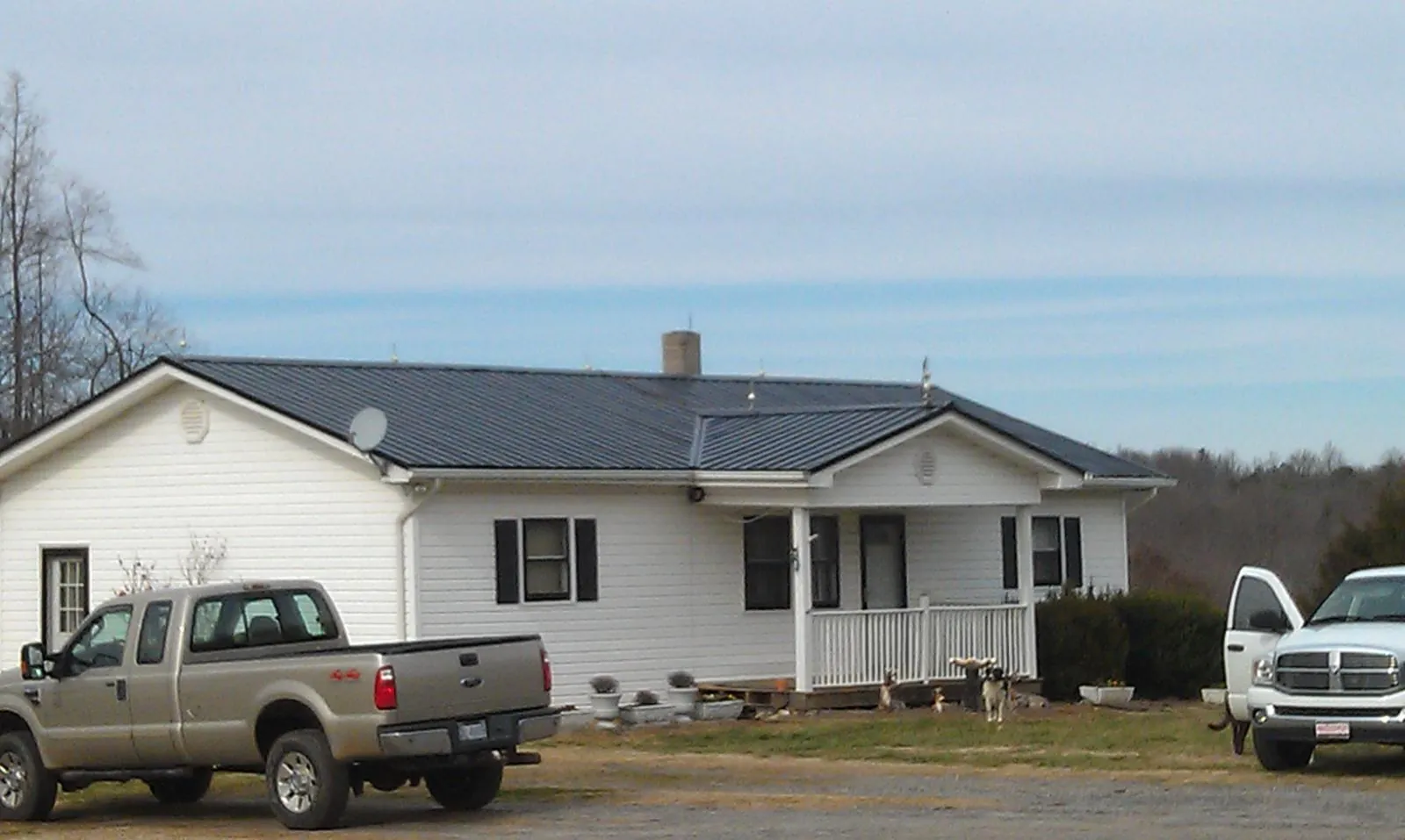 Finished dark metal roof on a white ranch home with work trucks parked in Bunch